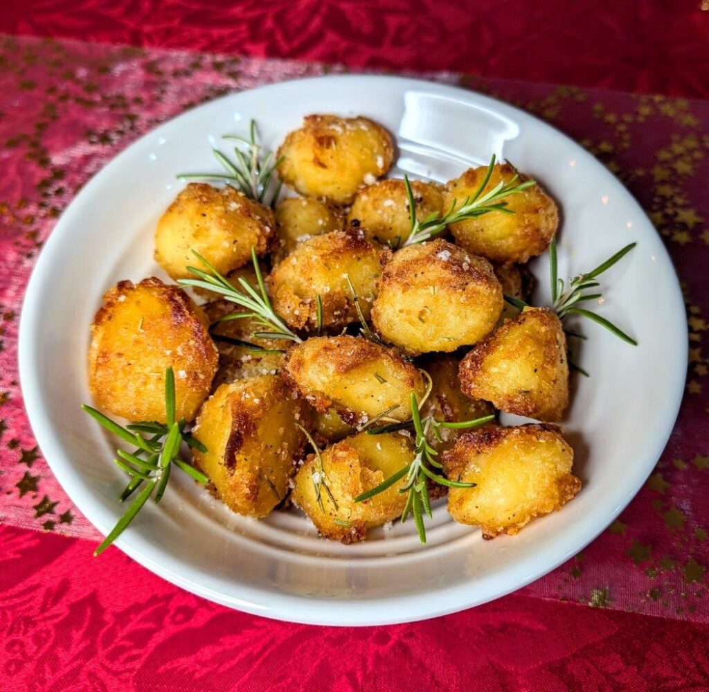 A bowl of crispy roast potatoes with golden brown exteriors, topped with flaky salt and rosemary sprigs
