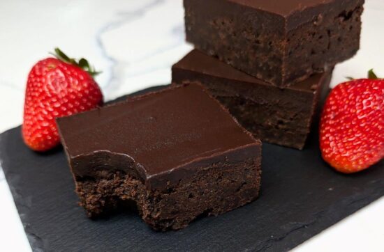 A pile of chocolate brownies with a smooth Kahlua ganache served on a stone board with strawberries
