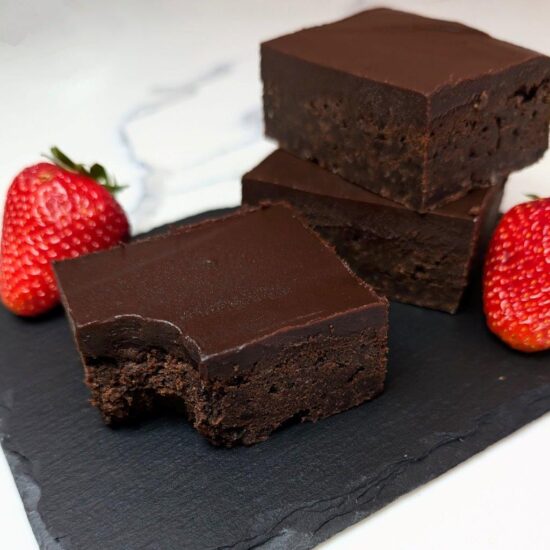 A pile of chocolate brownies with a smooth Kahlua ganache served on a stone board with strawberries