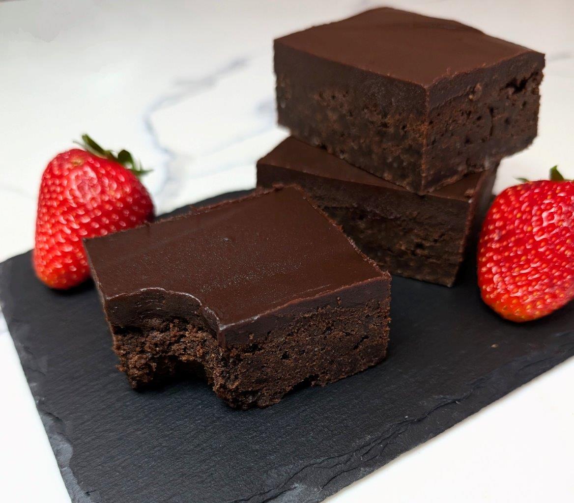 A pile of chocolate brownies with a smooth Kahlua ganache served on a stone board with strawberries