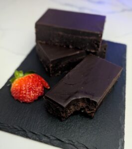 A pile of chocolate brownies with a smooth Kahlua ganache served on a stone board with strawberries