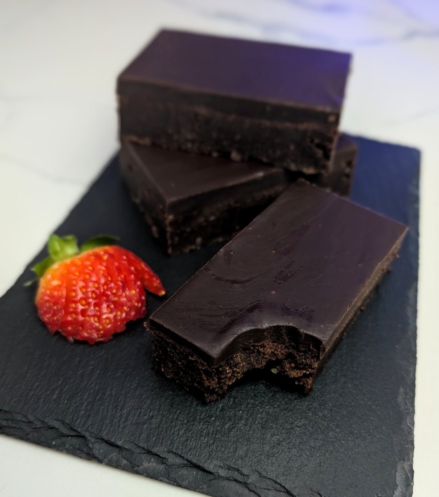 A pile of chocolate brownies with a smooth Kahlua ganache served on a stone board with strawberries