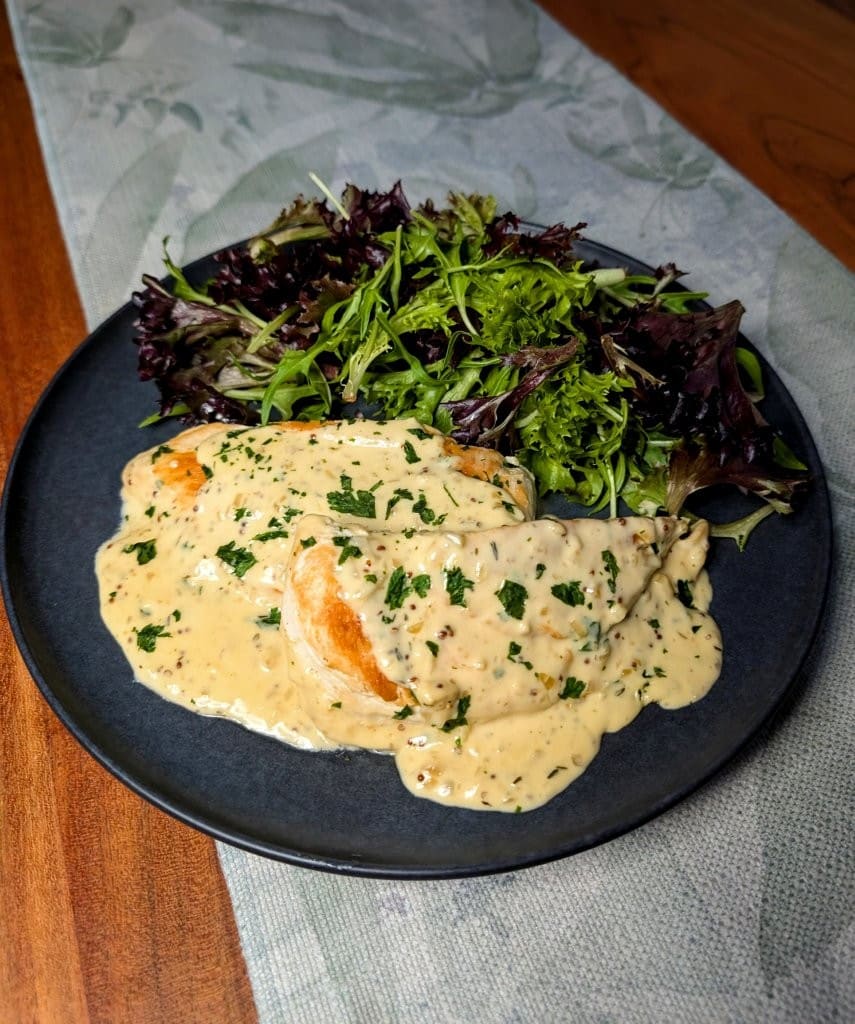 A serving of golden chicken breast topped with thick and creamy mustard sauce