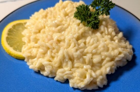 Bright creamy lemon risotto served on a striking blue plate, topped with a parsley sprig and with a slice of lemon on the side