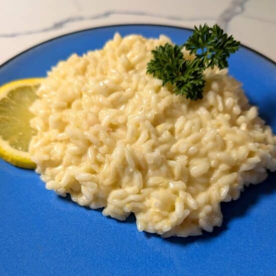 Bright creamy lemon risotto served on a striking blue plate, topped with a parsley sprig and with a slice of lemon on the side