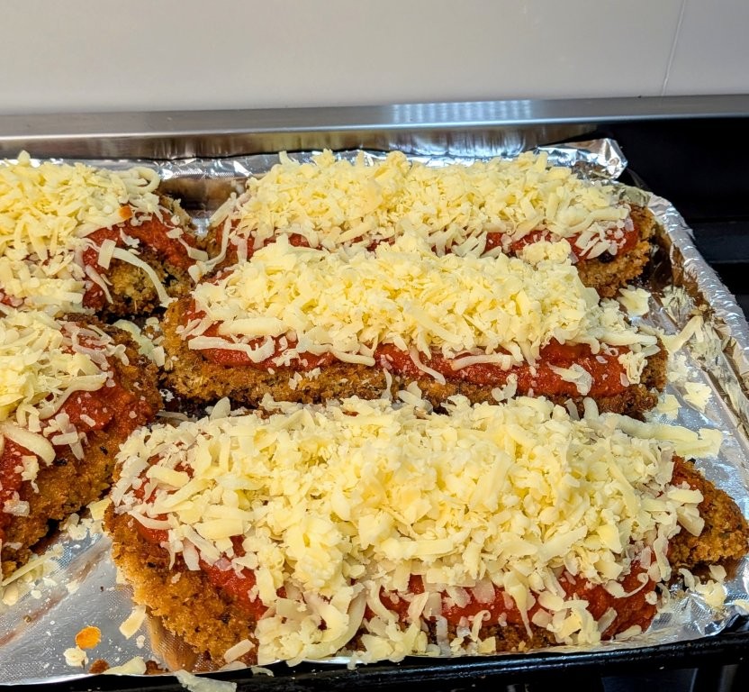 Shredded cheese piled on top of chicken schnitzels and napoli sauce, ready to bake