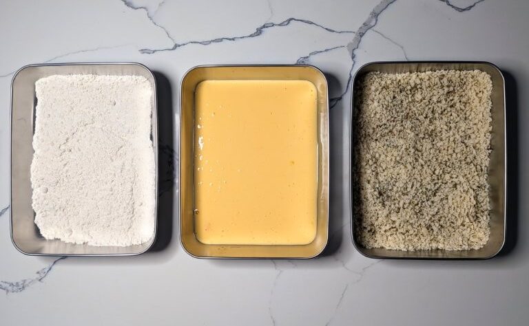 A breadcrumbing station with 3 bowls; from right to left: flour, egg wash, breadcrumbs