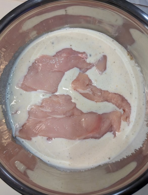 Chicken breasts in a large bowl with a buttermilk and herb marinade